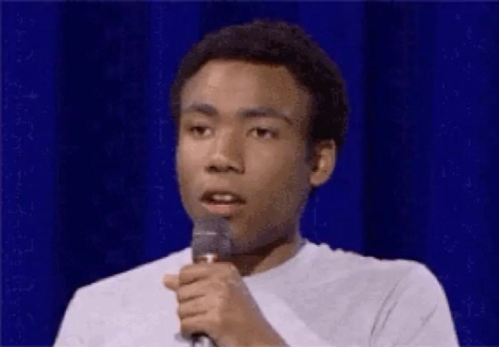 a man is holding a microphone in front of a blue curtain and talking into it .