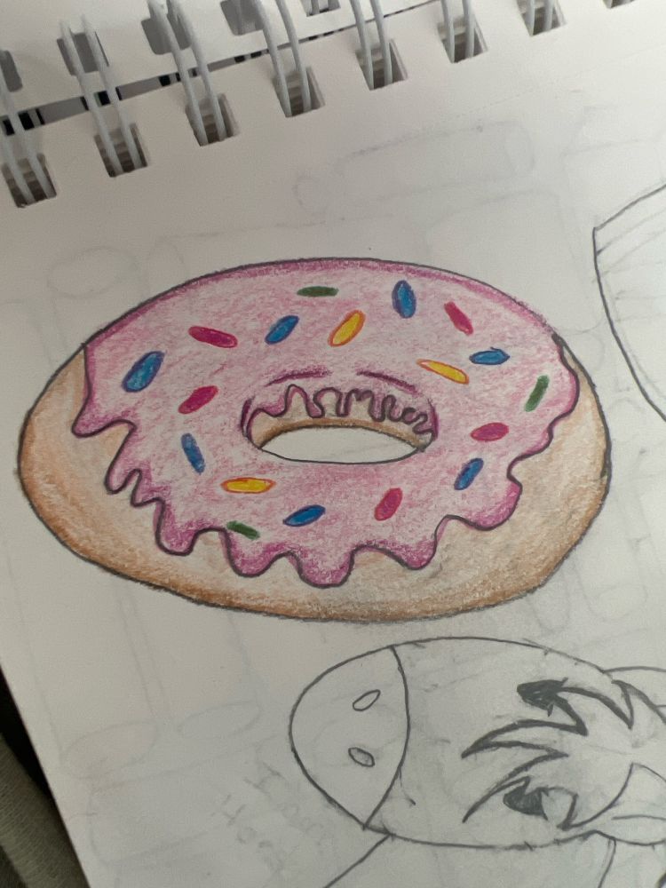 A beginners drawing of a donut with pink icing and sprinkles. The drawing is in a sketch pad and the coloration is made with soft, colored pencil. The drawing out of the main frame and to the bottom is a simple, cartoon drawing of a horse head. Above the drawing, at an angle, the white spirals of the sketch book can be seen. 