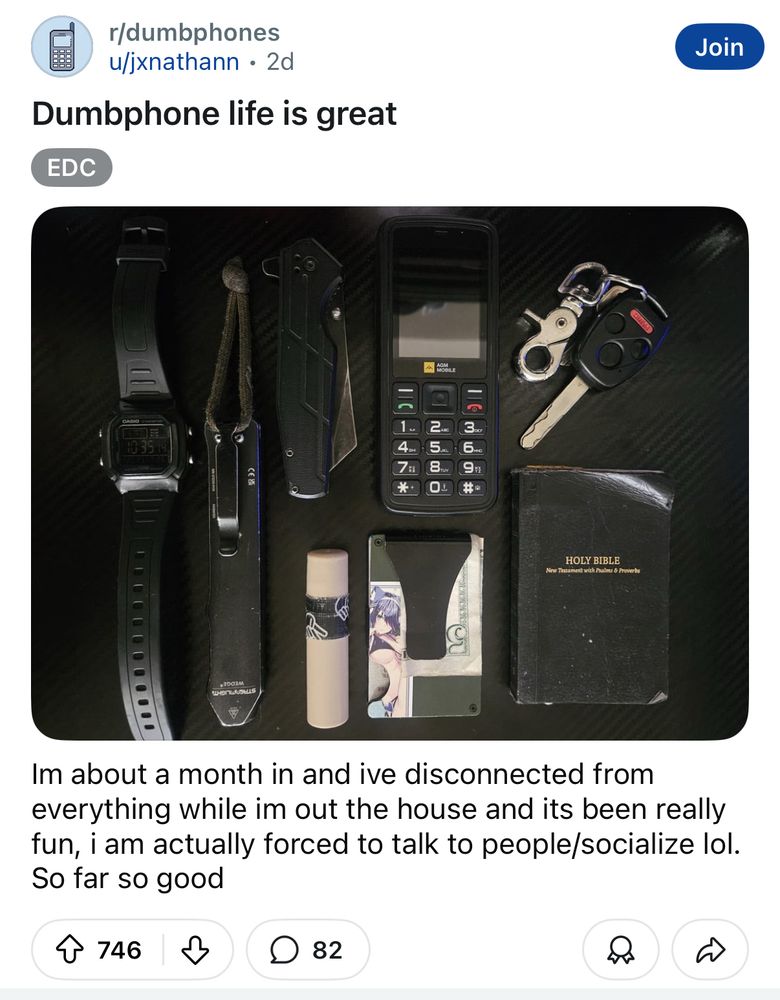 reddit post on r/dumbphones titled “Dumbphone life is great”, reading “Im about a month in and ive disconnected from everything while im out the house and its been really fun, i am actually forced to talk to people/socialize lol. So far so good” 

a photo is attached showing a feature phone, some other everyday items, a wallet with a decal of an anime-style catgirl in a bikini, and a copy of the new testament 