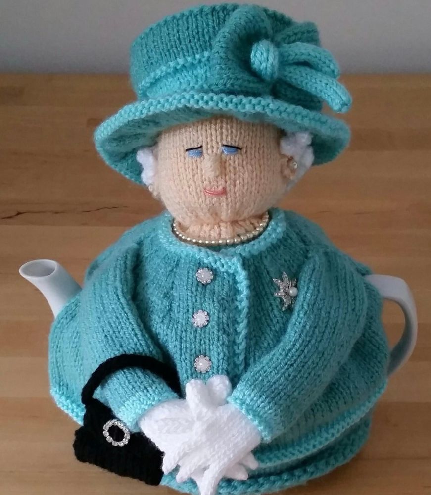 An amusing, hand-knitted tea cozy in the style of Queen Elizabeth II wearing a turquoise jacket and matching hat, white gloves and carrying a handbag.