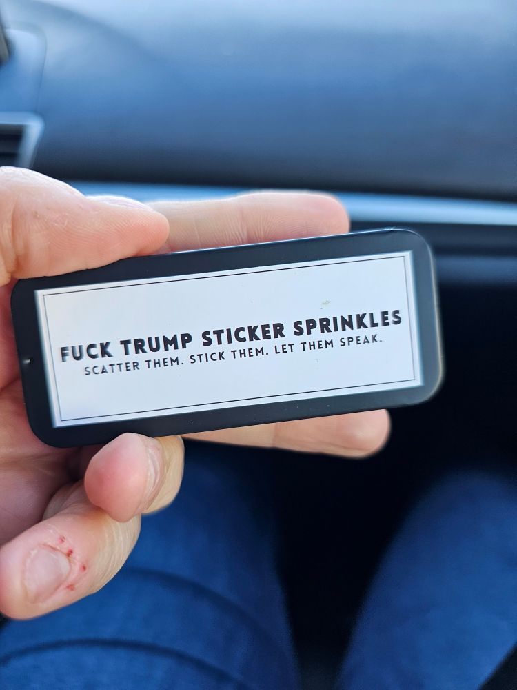 A small black Altoid style tin with a white label that says "Fuck Trump Sticker Sprinkles - Scatter Them. Stick Them. Let Them Speak."