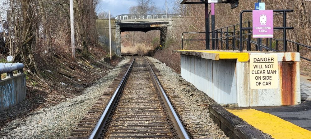 Commuter rail line, overpass in the distance. Sign reads, " DANGER WILL NOT CLEAR MAN ON SIDE OF CAR"