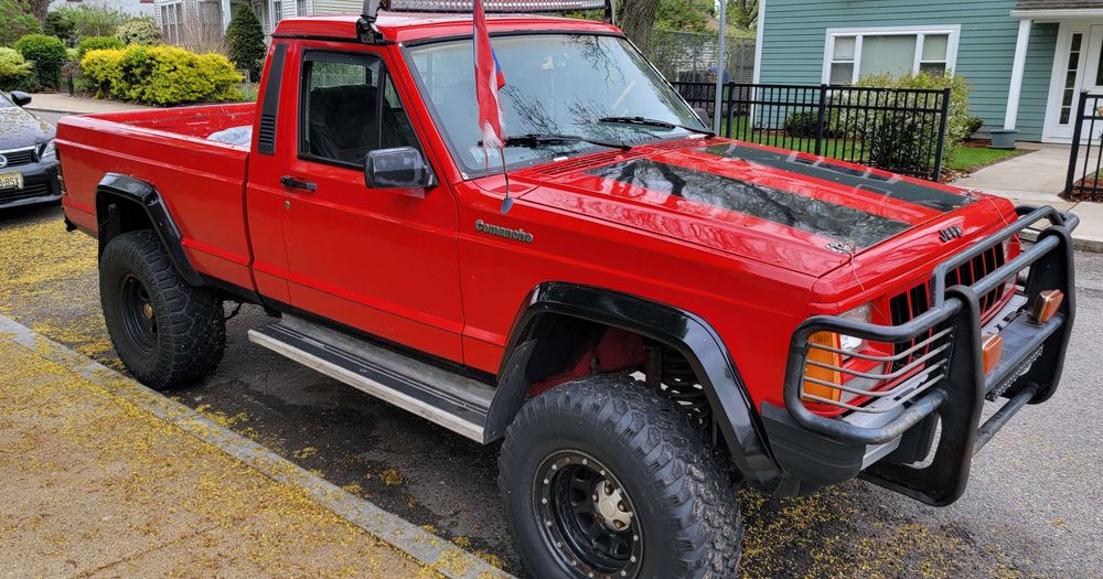 Red Jeep Commanche, maybe 1989 or later. What looks like a Puerto Rican flag hanging from the antenna. I love this truck (not mine). My first vehicle was a heavily used 86 Dodge Ram 50 that essentially was a rebadged Mitsubishi.