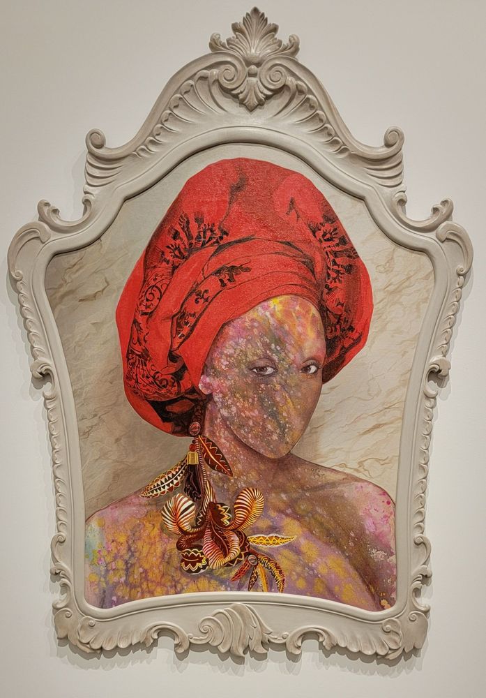 Firelei Báez - given the ground (the fact that it amazes me does not mean I relinquish it). An unusually shaped framed canvas centered around the portrait of a woman with kaleidescape skin, piercing eyes, and an ornate head wrap with dangling feather accessories