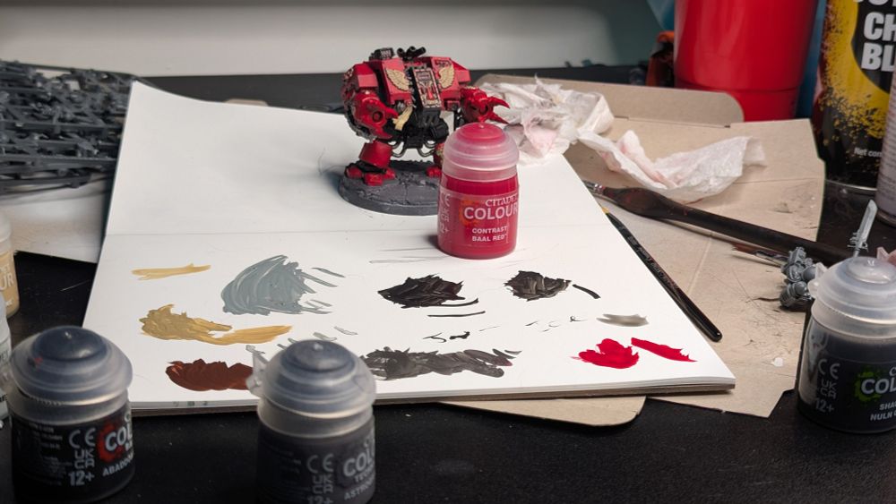 A blood angels dreadnought with various tubs of paint around him