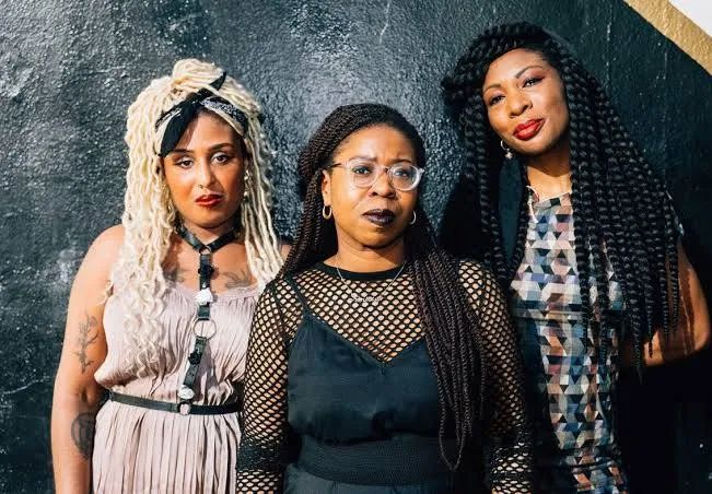 “Big Joanie is a British punk band formed in London in 2013. Its members are Stephanie Phillips (guitar and vocals) and Estella Adeyeri (bass guitar and vocals). Founding drummer Chardine Taylor-Stone left the band in 2023.” Image shows the three original members 