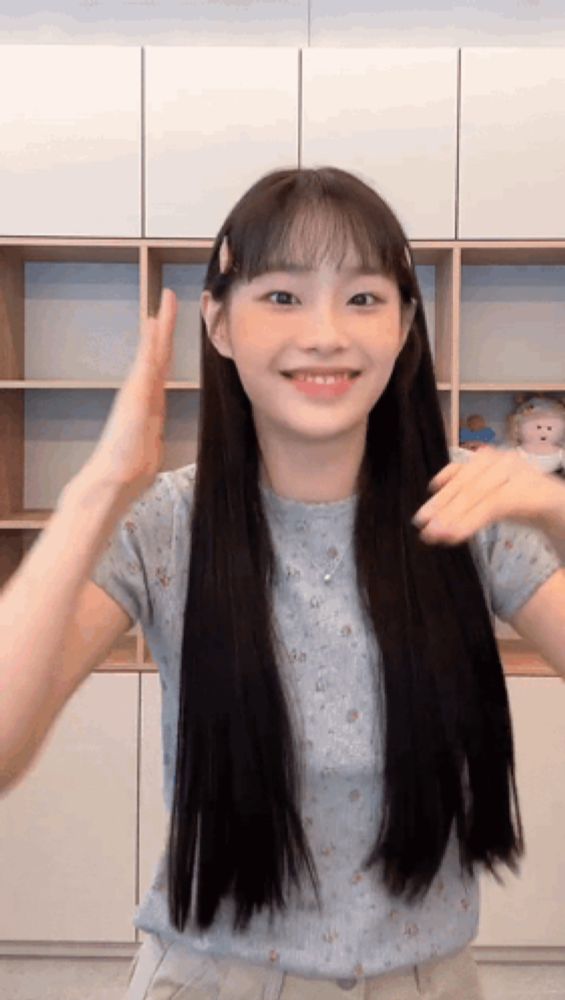 a young girl with long black hair is giving a high five in front of a shelf .