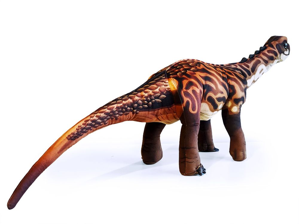 A realistic depiction of a baby Diplodocus dinosaur. The colouration is a striped brown and deep orange. It has scales along it's tail, which is visible because the plush looks away from the camera.
