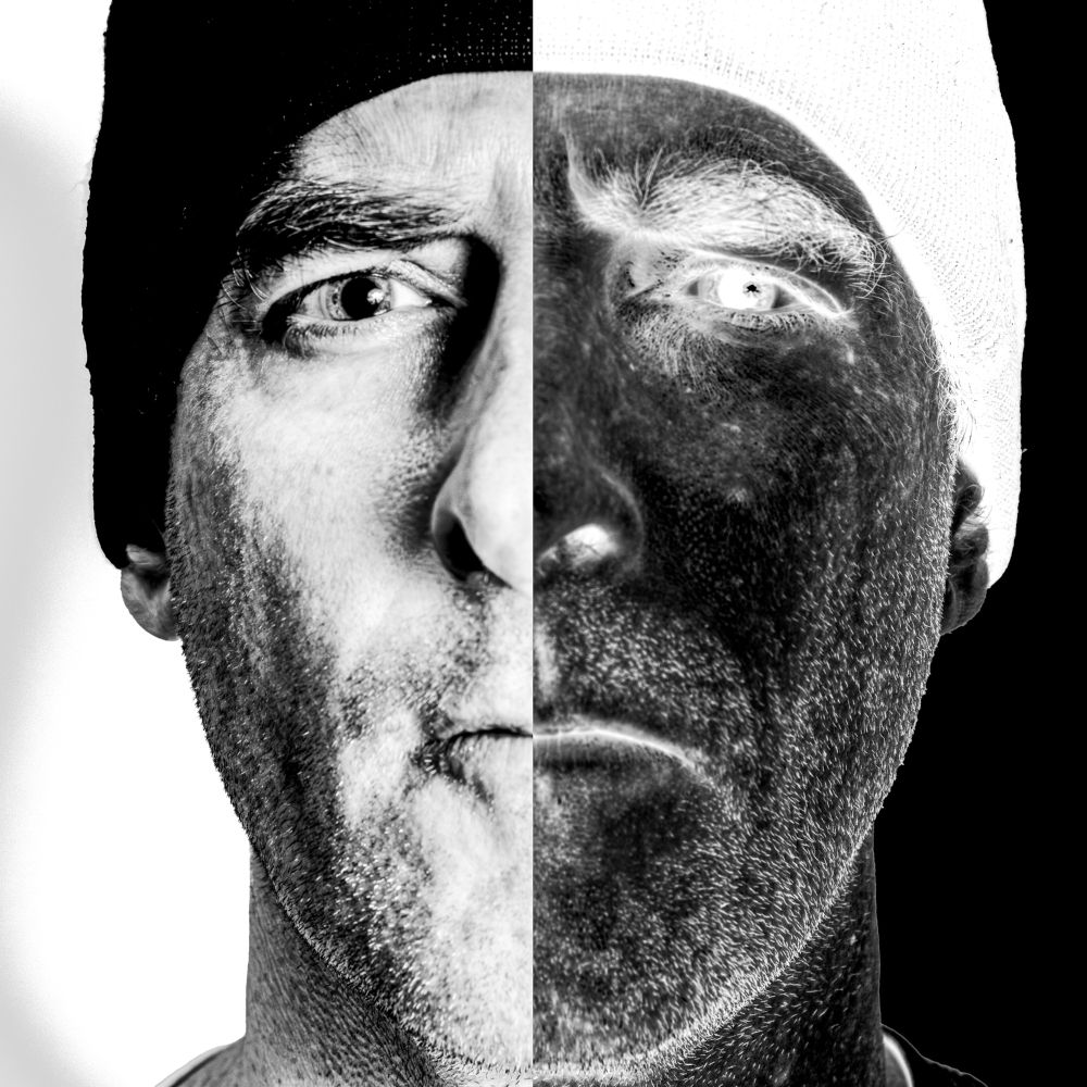 A square self-portrait with the face filling most of the space. The image is high contrast monochrome and divided in two, vertically. The left side is a normal exposure of a caucasian man with a white background and black knit hat. The right side is a negative exposure of the same - the hat is bright white, the background completely black, and the face dark.