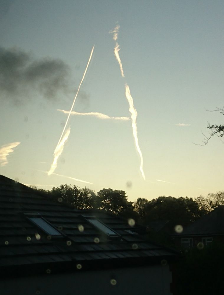 A shaped contrail light up by the sun, taken through a window with rain spots at the bottom 