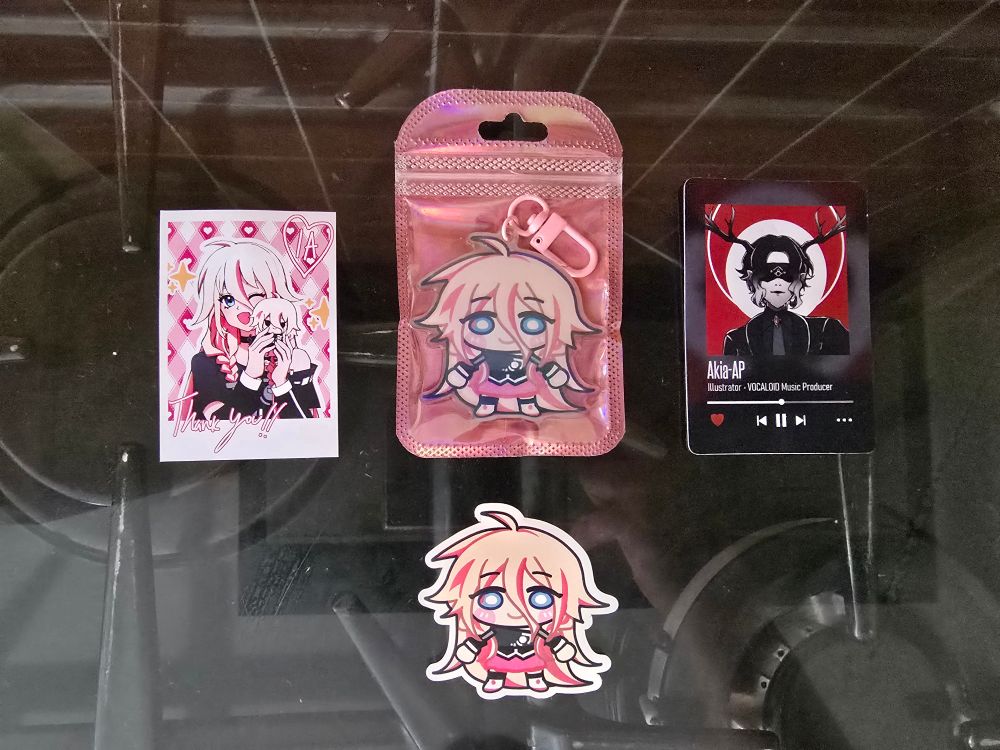A photograph of the IA keychain and sticker by Akia-AP, as well as a small thank you card and their business card
