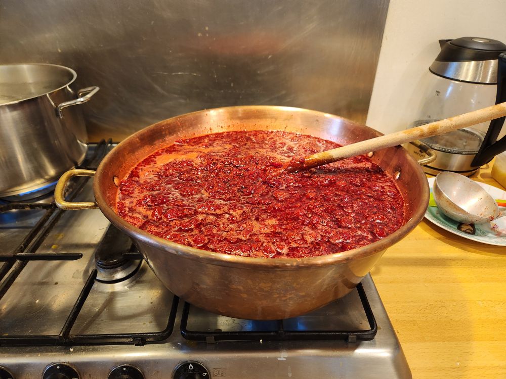 Bassine en cuivre sur une gazinière, dedans il y a de la confiture de framboises en cours de cuisson. 