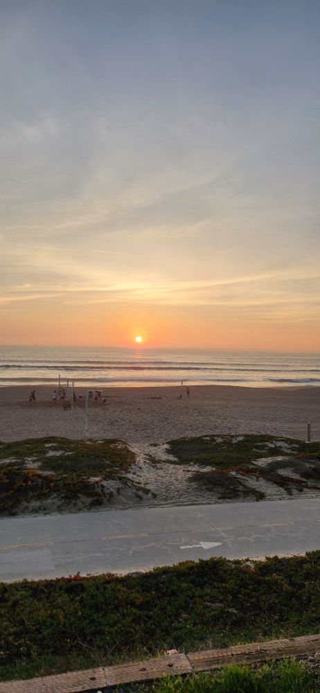 Sunset at the beach, light blue greyish skies, folks playing volleyball on the beach