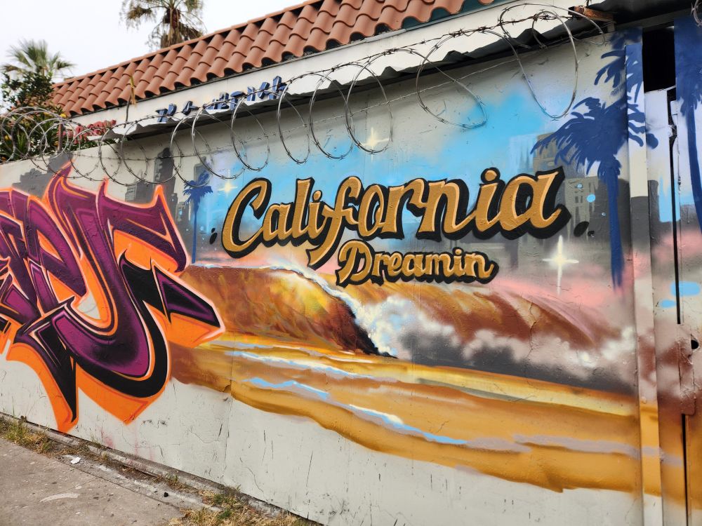 Street art, depiction of a skyline, palm trees and waves overlay text says California Dreamin' 