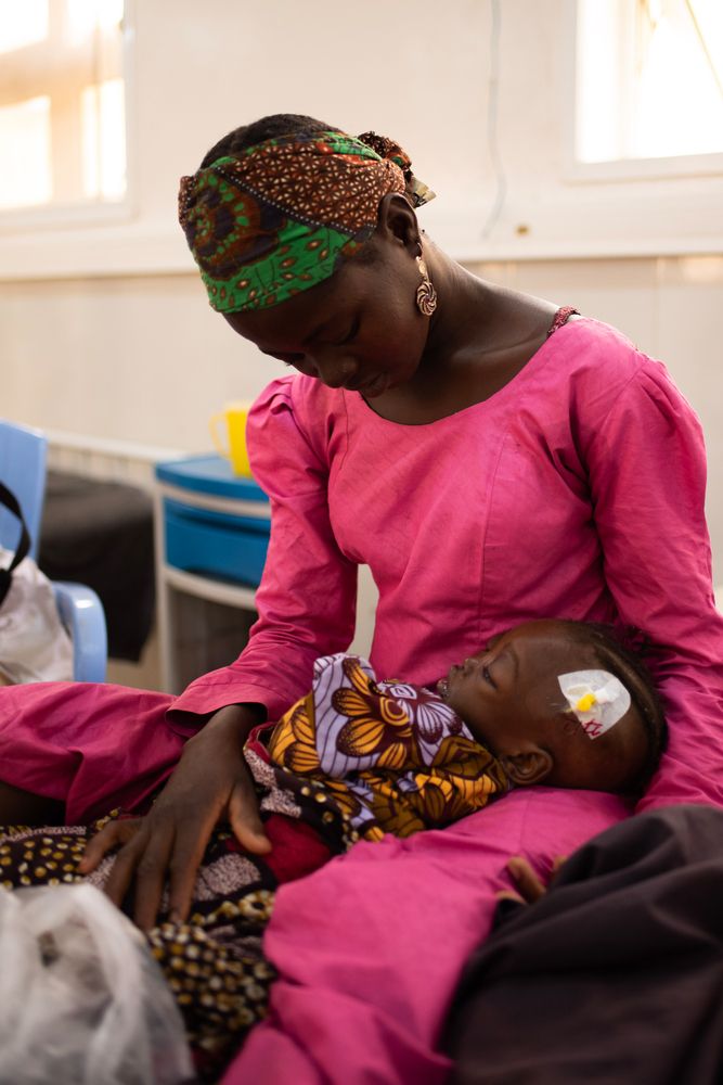 Musiaba Gidado sostiene a su bebé Fátima, que se está recuperando en el centro de alimentación para pacientes hospitalizados de la ciudad de Katsina. Fátima padece desnutrición grave y complicaciones como edema, lo que le ha provocado hinchazón en la cara y las piernas y mucho dolor.
Foto de Zoe Bennell/MSF