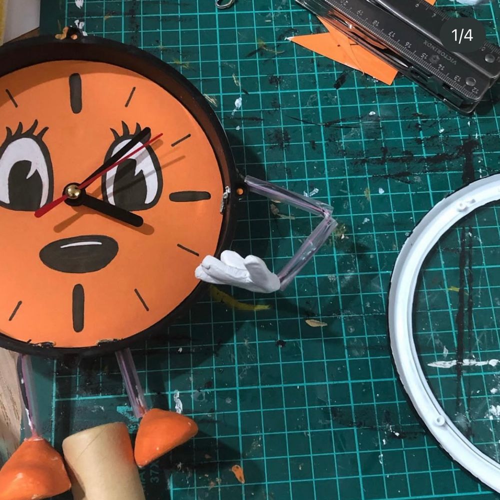 Miss Minutes prop made out of a clock, orange cardboard, pens, paints, paper clay, wire and a straw