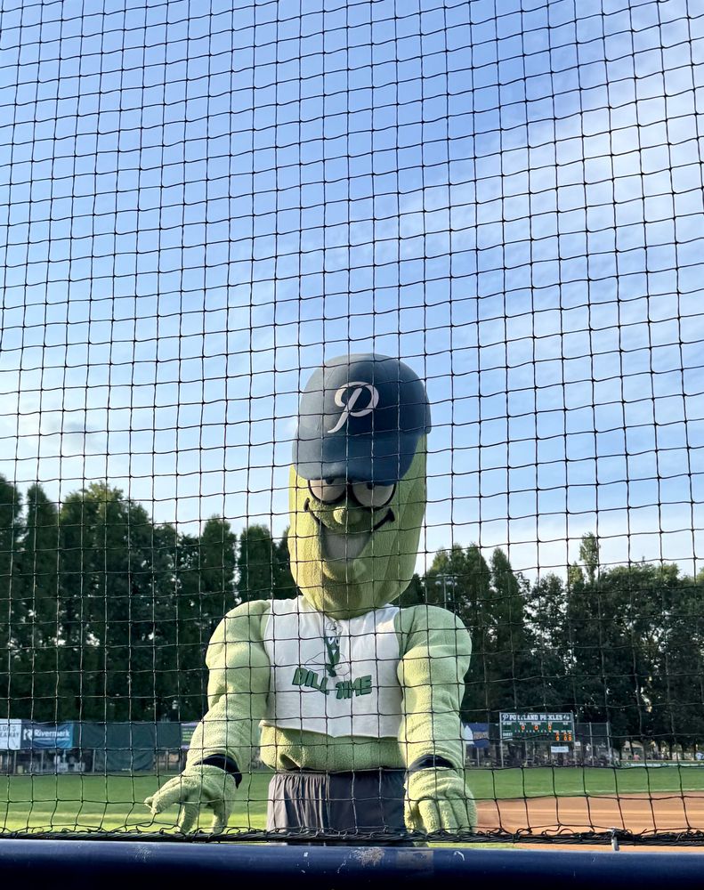 Dillon T Pickle (giant pickle mascot) wearing a Dill Time crop top, on the baseball field, posing for a picture. 