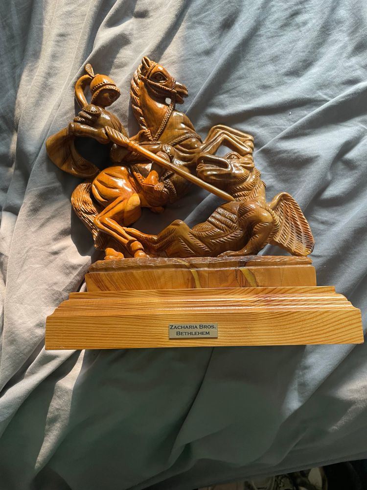 Wooden sculpture of a knight on a rearing horse pushing a sword through the heart of a dragon 