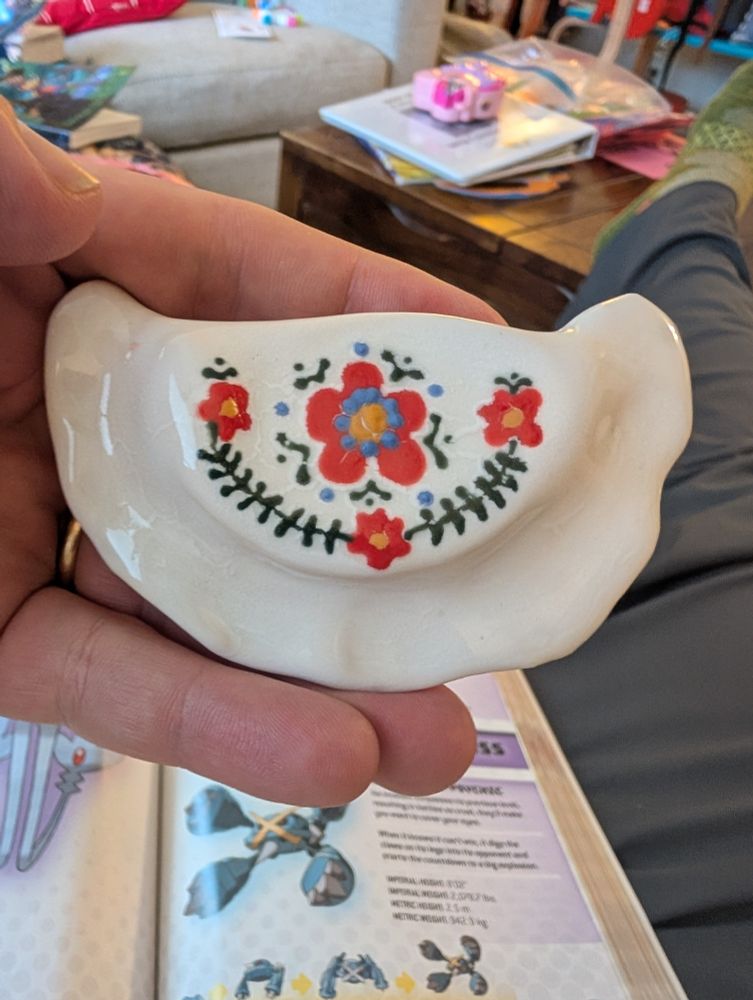 A ceramic pierogi with flowers and vines painted on reminiscent of polish folk art patterns. 