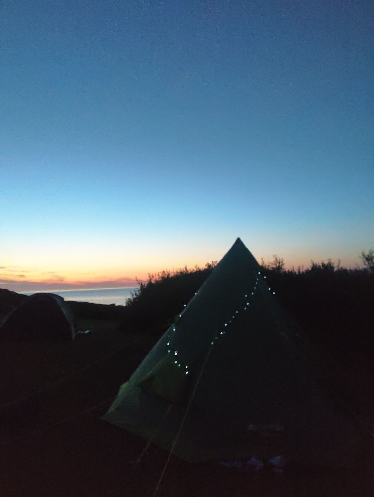 A tipi-style tent adorned in fairy lights set against a hazy summer sunset.