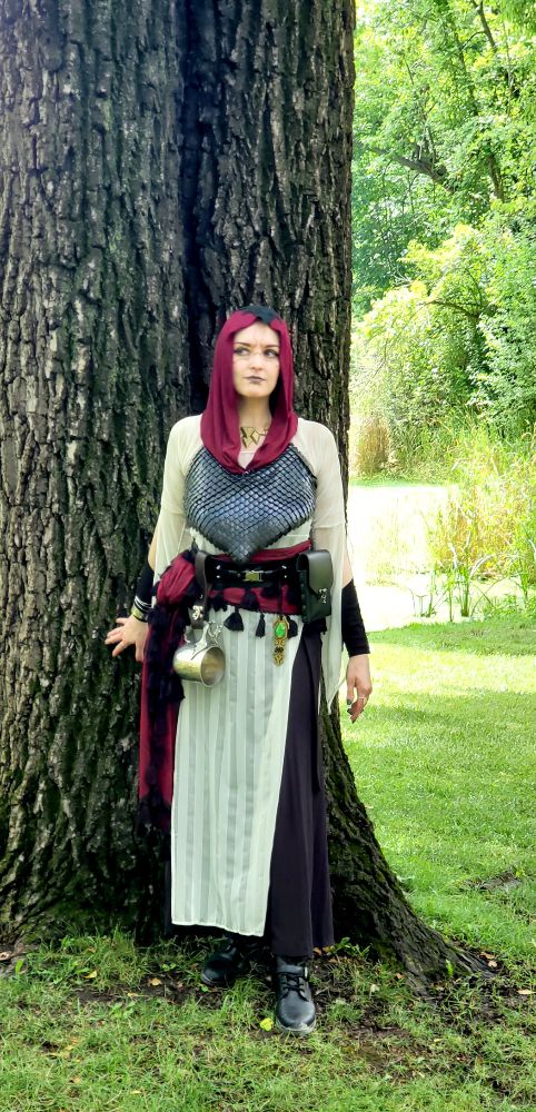 A front-on photo of widgetoc in her Faire Merrin. She has her back to a tree and is glancing off to her right. 
