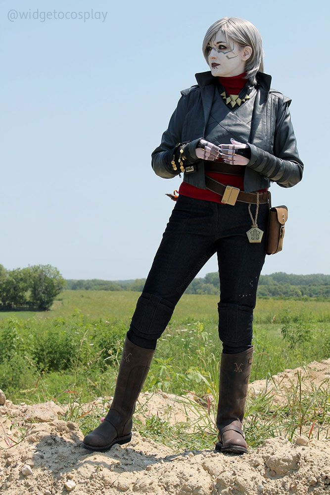 Cosplayer @widgetoc cosplaying as Nightsister Merrin from the video game Jedi: Survivor. She appears to be listening to someone off-screen and while standing on dirt in a prairie that looks a little like a flatter version of the planet Koboh. 