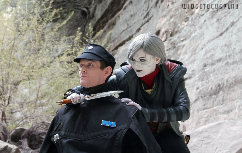 Cosplayer widgetoc dressed as Nightsister Merrin, confidenly holding her dagger to the surprised throat of cosplayer masterente, who is dressed as an Imperial Officer. Conveniently, he is wearing a poncho that she intends to bring back for her Jedi friend and poncho aficionado, Cal Kestis. 