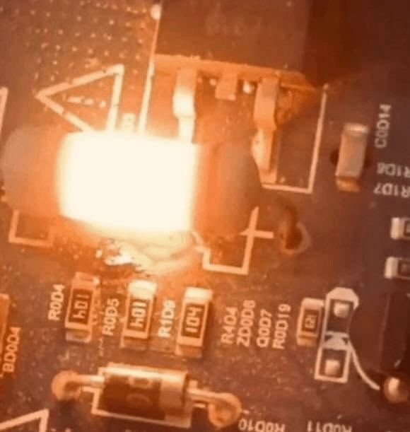 Ein elektronisches Bauteil (Widerstand) auf einer Platine glüht hellorange aufgrund starker Überhitzung; umliegende Bauteile und Leiterbahnen sind sichtbar.