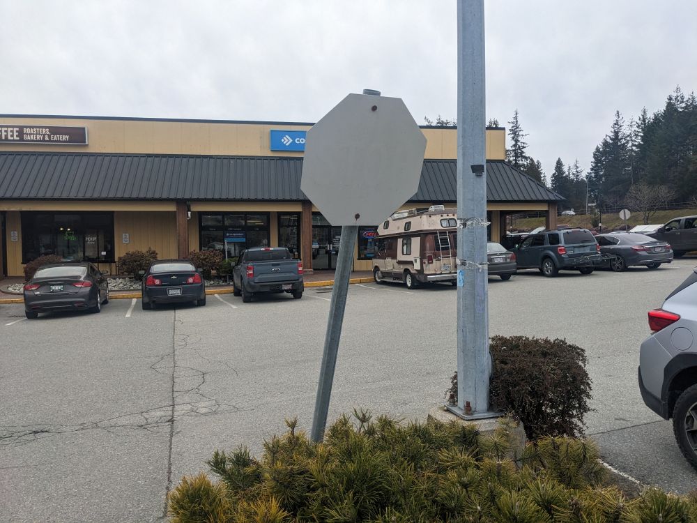 A stop sign in parking lot that's been bleached by the sun and stands crooked, bent forward by the weight of watching fools in cars for too long