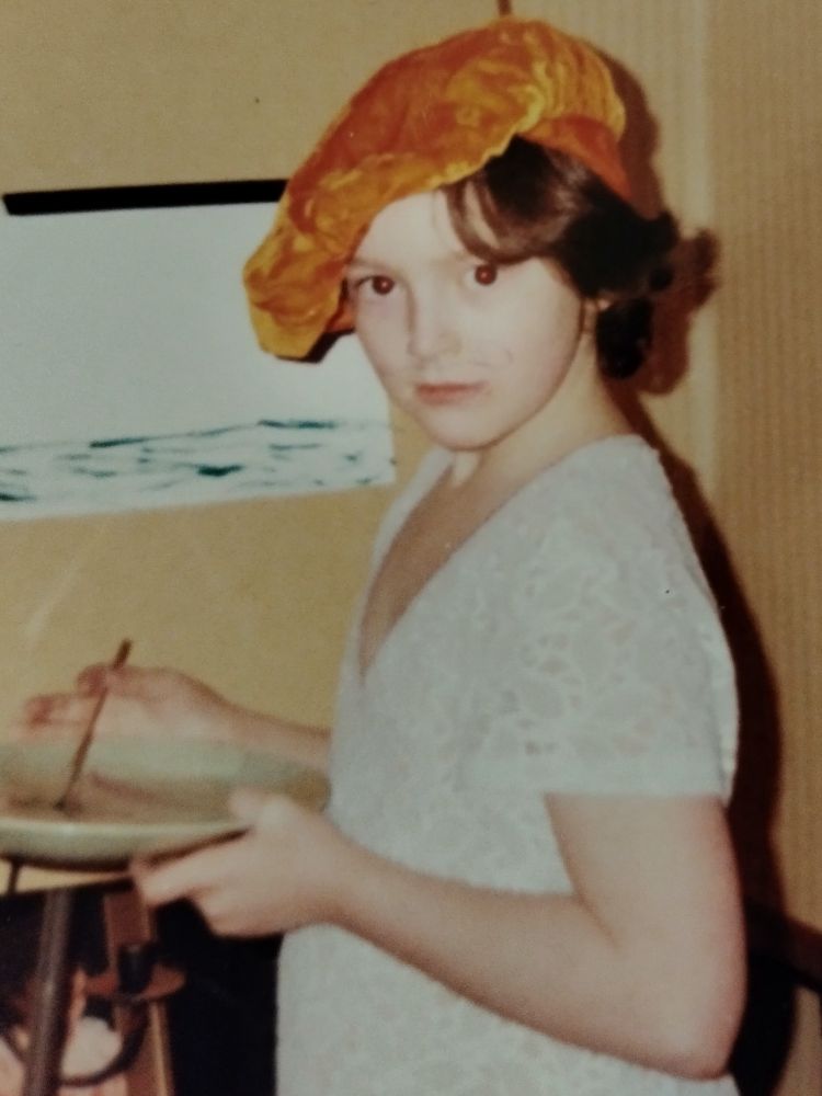 child painting on an easel, wearing an orange beret + with a curly moustache painted on their face