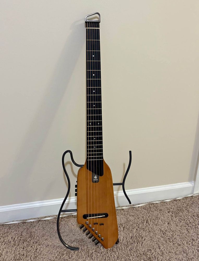 Acoustic electric guitar with no headstock and a very small body design and metal handles mounted around the body.