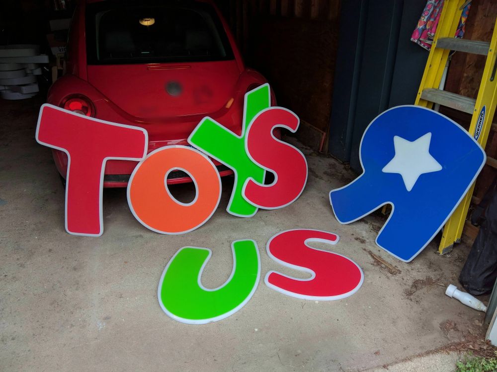 the letters from the Toys 'R' Us store sign, laying inside a garage on the side of a car for scale. they are about 4 feet tall