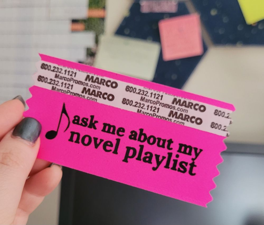 A bright fuschia ribbon with the text "ask me about my novel playlist" and a music note symbol in black.
