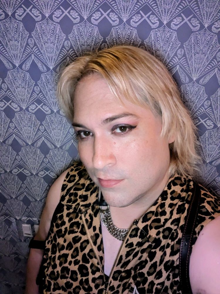 Blonde in a sleeveless leopard jumper wearing a leather and chain collar. 