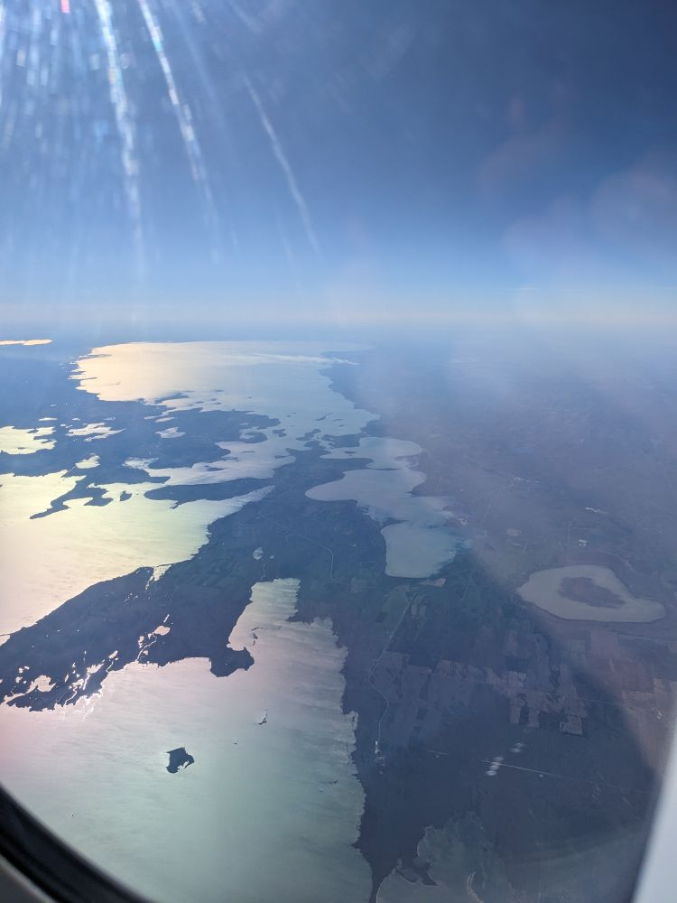 View from plane window: flat plains, farms, lakes reflecting yellow sunlight