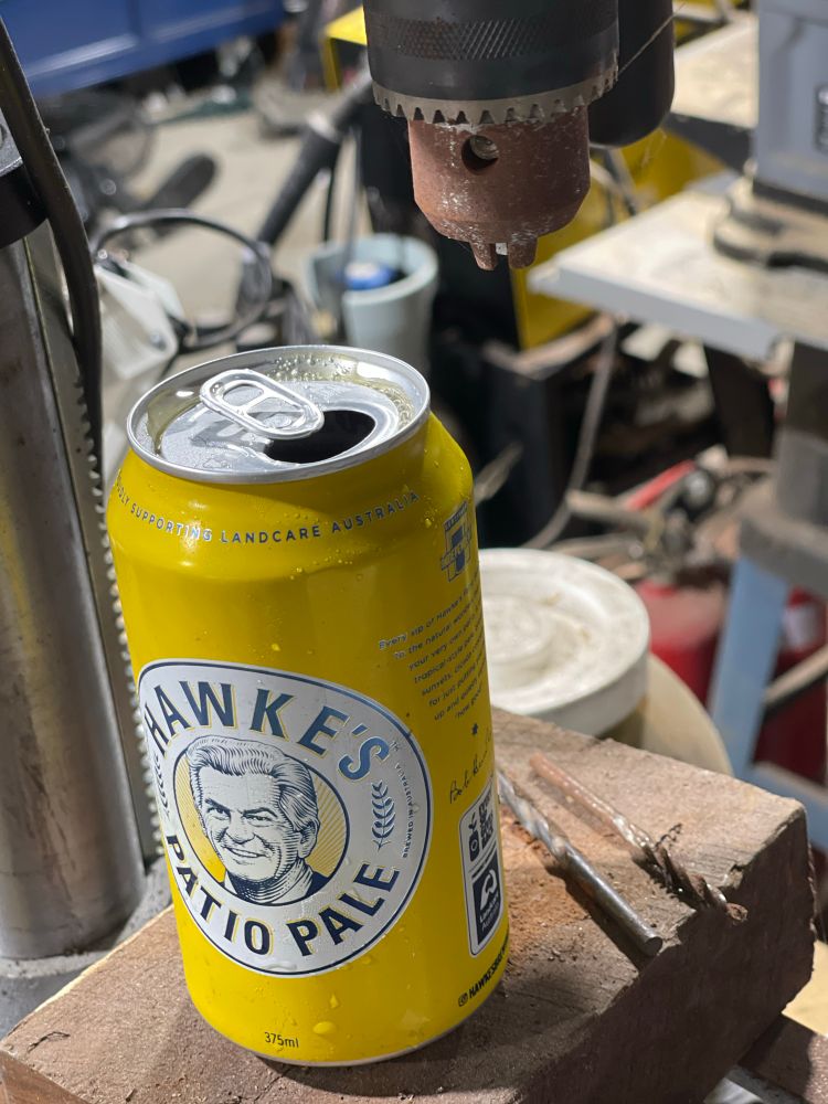 A can of Australian beer on a drill press in a dusty shed 