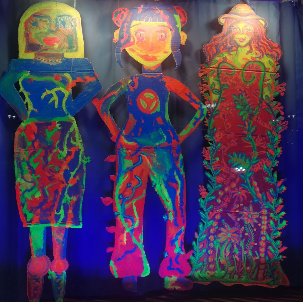 Kolme värikästä, uv-valoista naishahmoa.