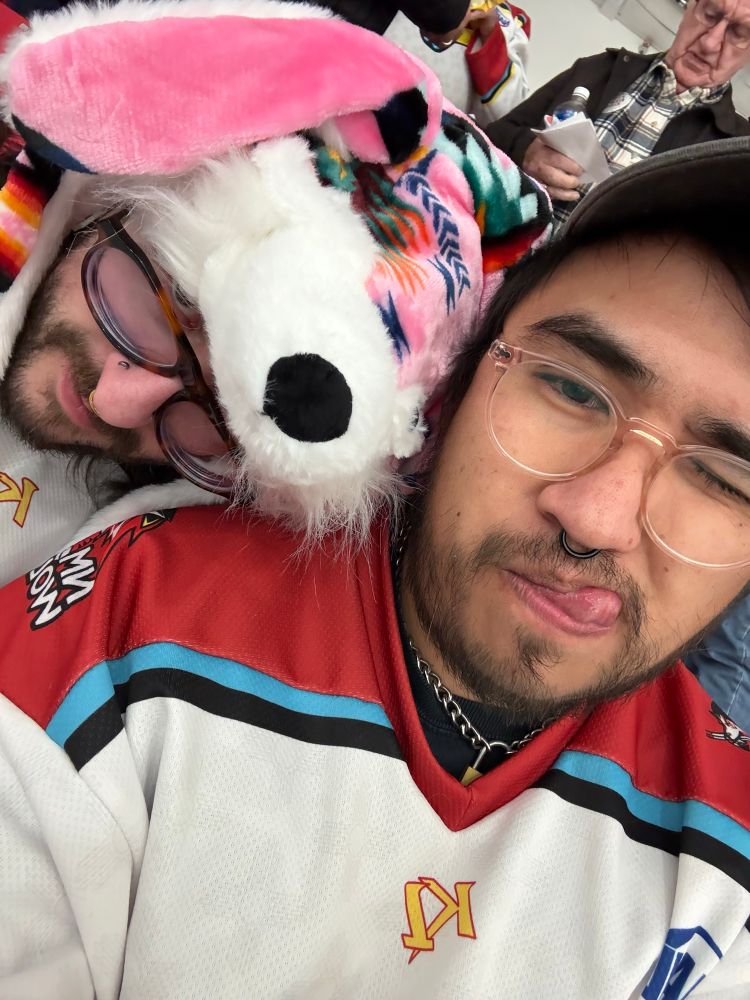 Kiebe with a pink wolf hat and monkey sticking their tongue out while at a hockey game.