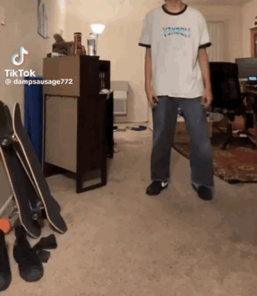 a man in a white shirt is standing in a room with skateboards on the floor