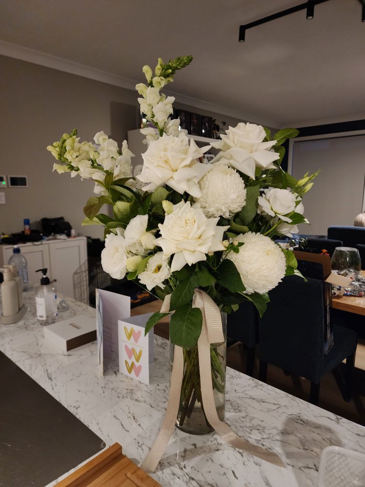 Tall vase of various white flowers including roses, lissianthus, chrysanthemums maybe? And something that could be stocks? (Sorry I'm not good at flower identification.)  Also greenery. 