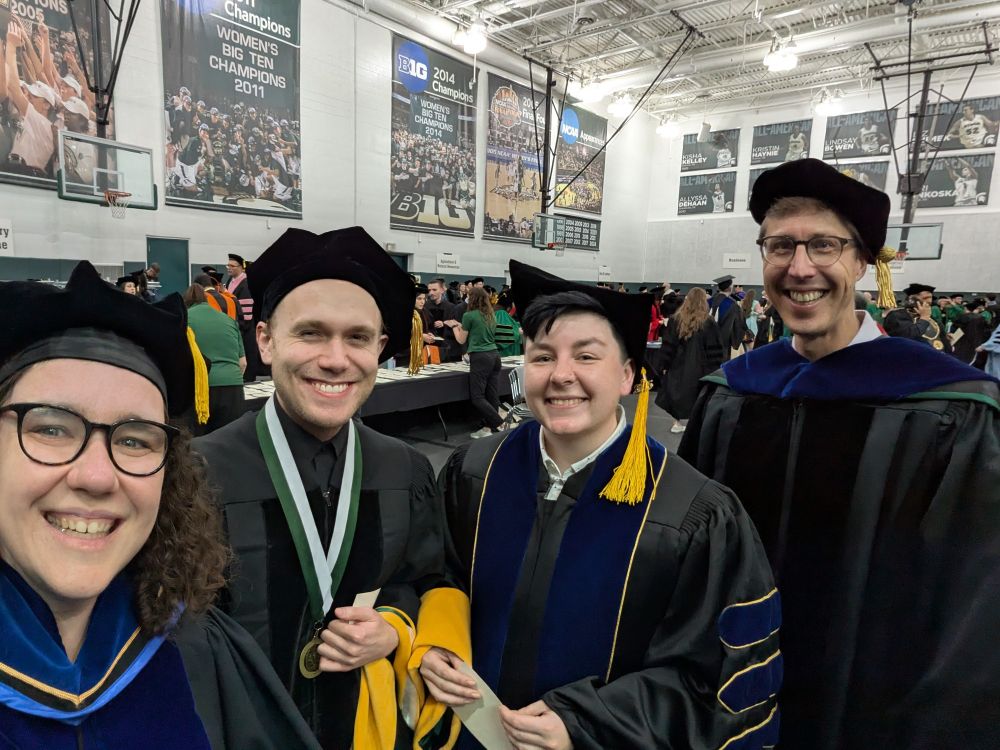 Four smiling scientists in graduation robes.