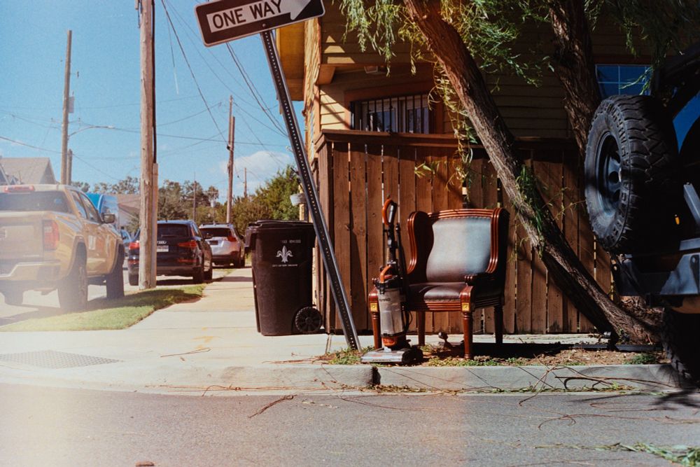 Chair and a vacuum sitting curbside next to a one way sign