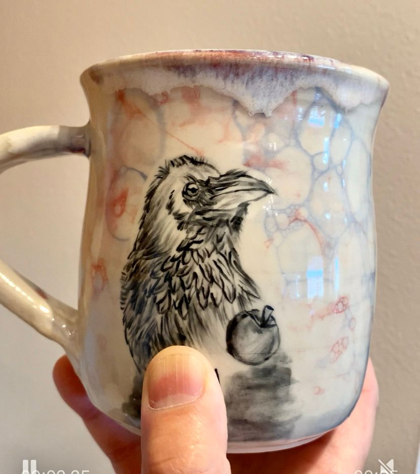 Hand holding a ceramic mug with an image of a crow. 