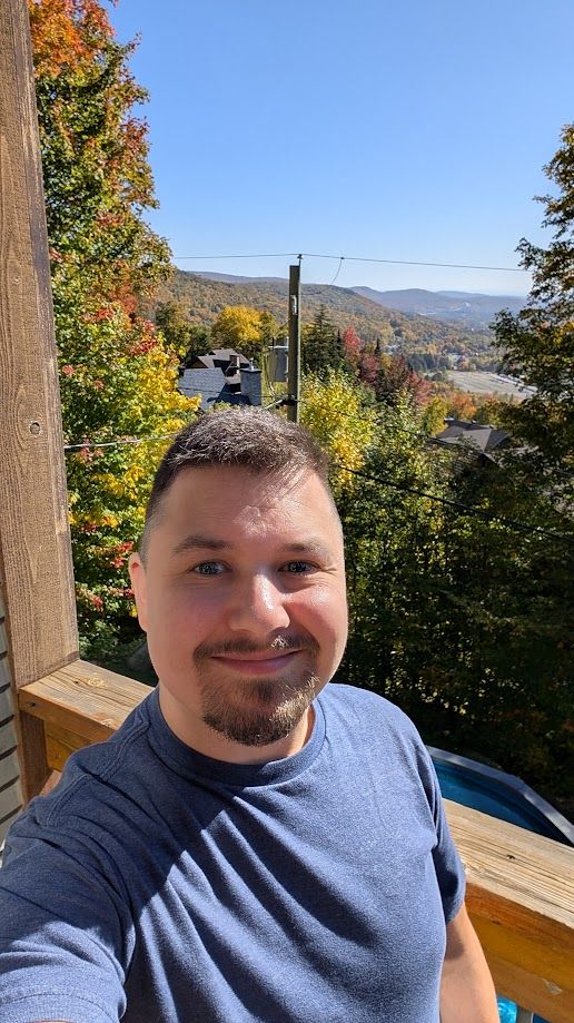 Picture of me in a blue t-shirt with a view of the mountain's valley behind me