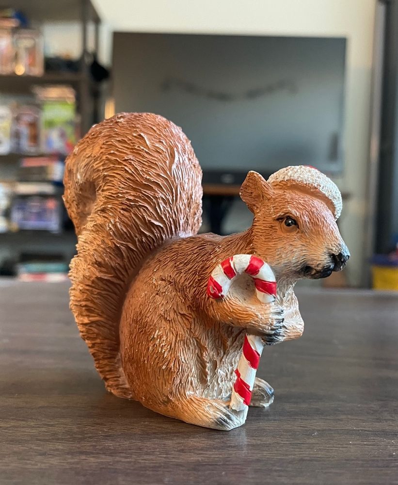 A small figurine of a grumpy looking squirrel clinging to a large candy cane 