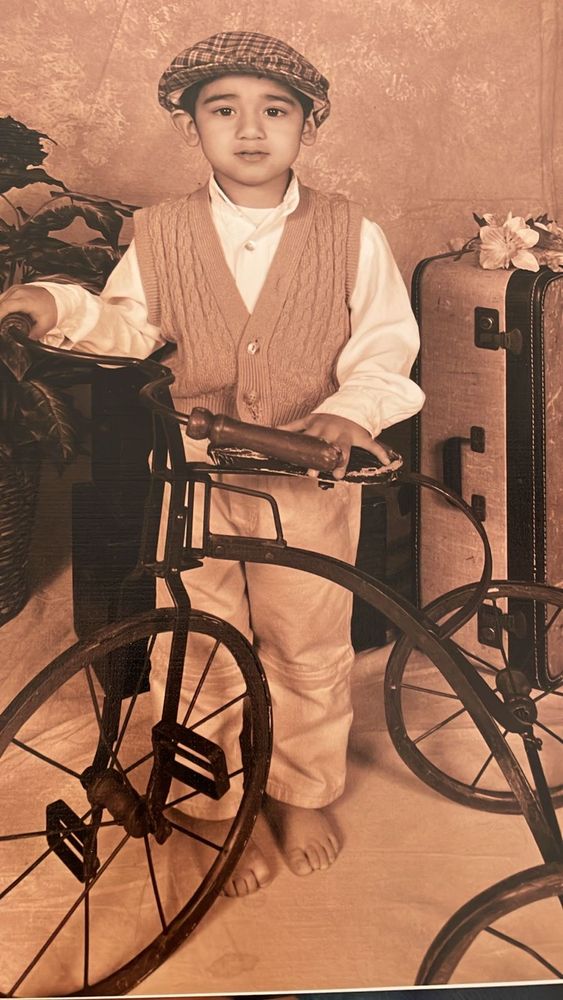 Alt-text: Sepia-toned portrait of a barefoot boy in vintage clothing beside an antique tricycle.