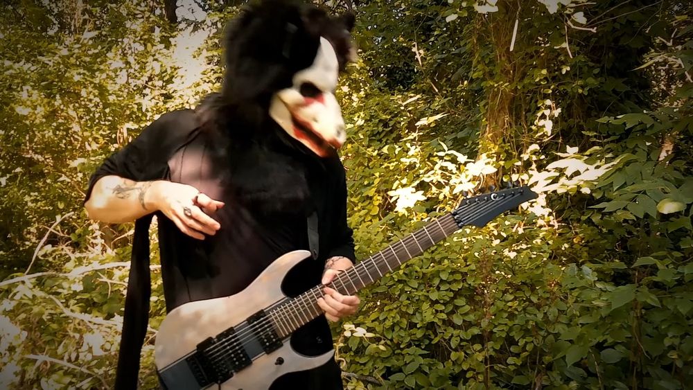 a skulldog wearing a black cloak with the sleeves pulled up. He's playing a guitar that looks almost like it's made of either stone or driftwood, with a black stripe down the center of it. He's bending a string up on the neck with his left hand, and his right hand is raised and it almost looks like he's pulling the music out of the guitar through magic or sheer will.