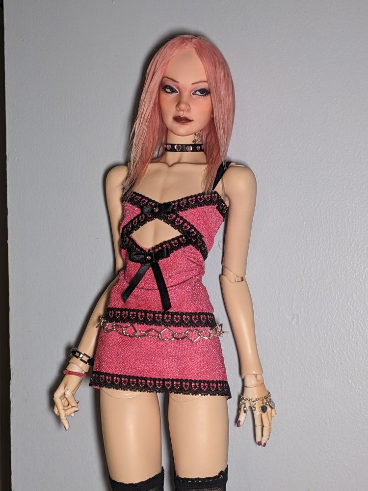 Picture of cal, a ball jointed doll that is styled to look like a Chinese man with long pink hair, posing in a pink dress with black lace details