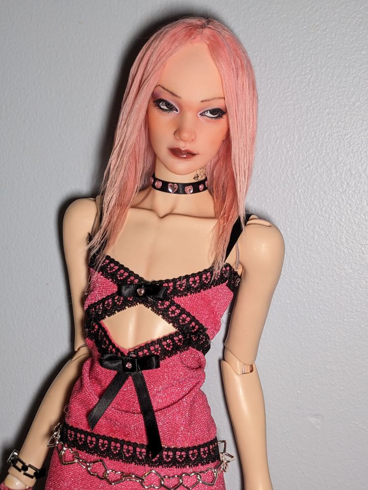 Picture of cal, a ball jointed doll that is styled to look like a Chinese man with long pink hair, posing in a pink dress with black lace details