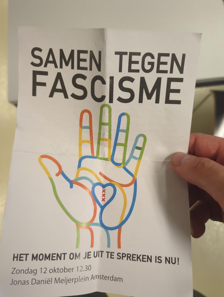 "Samen tegen fascisme".

Op de flyers staat een hand, getekend met lijnen van verschillende kleuren. In het midden van de hand zien we een hartje, met daarin de drie kruizen van Amsterdam.